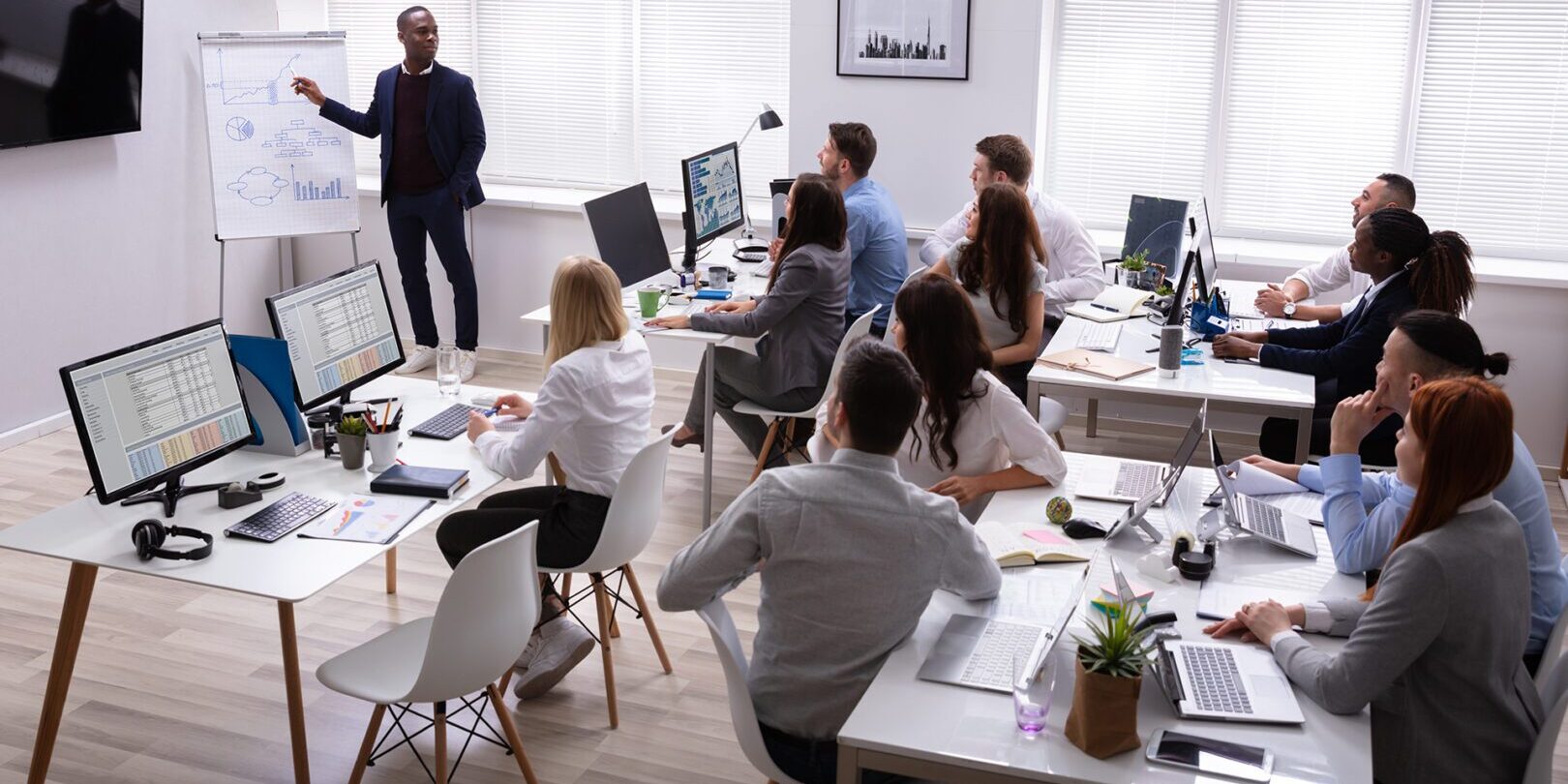 African Businessman Giving Presentation To His Colleagues Sitting On Table With Computers In Office