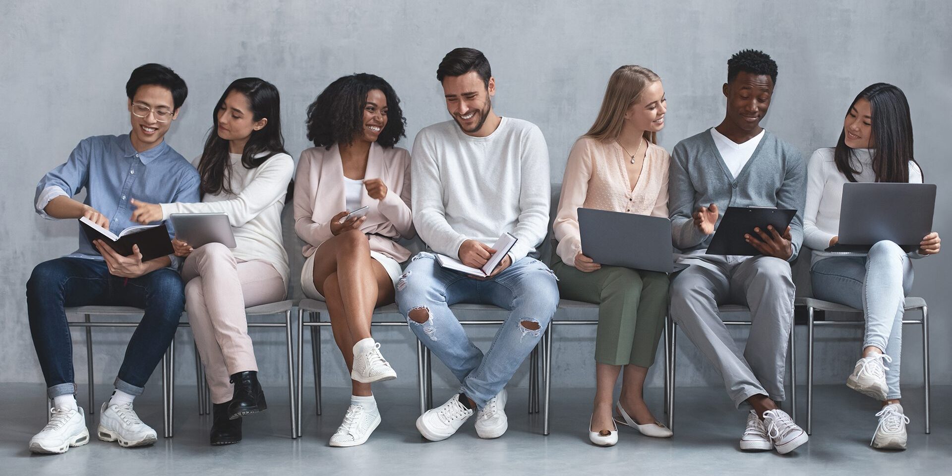 Group of multiracial young people waiting for job interview, talking to each other and smiling